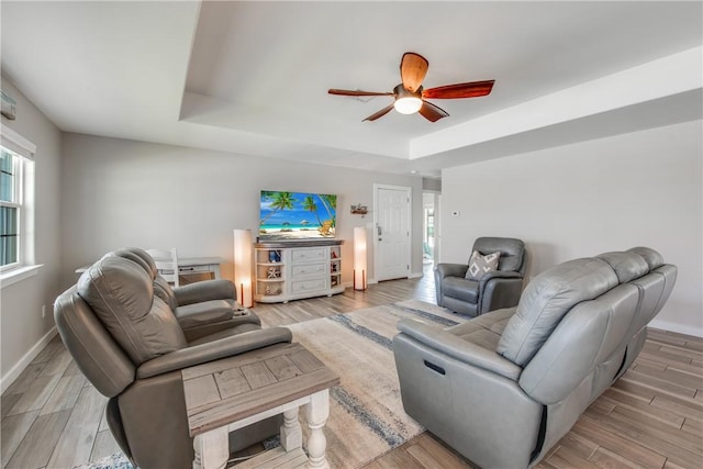 living room featuring light hardwood / wood-style flooring, a raised ceiling, and ceiling fan