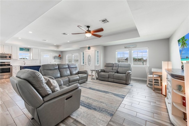 living room with ceiling fan and a tray ceiling