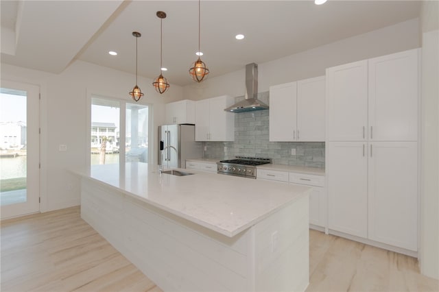 kitchen with light wood-type flooring, wall chimney exhaust hood, an island with sink, and high end white refrigerator