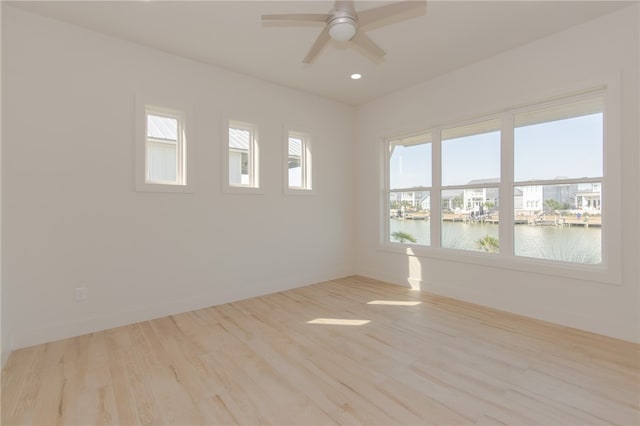 spare room featuring ceiling fan, a water view, and light wood-type flooring