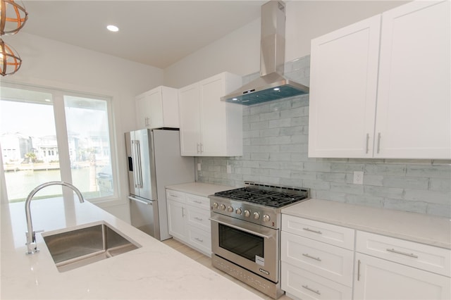 kitchen featuring white cabinetry, sink, appliances with stainless steel finishes, wall chimney range hood, and pendant lighting