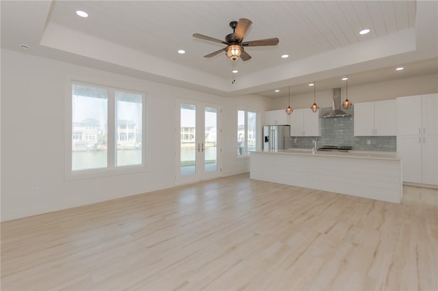 unfurnished living room with light hardwood / wood-style floors, ceiling fan, and a tray ceiling