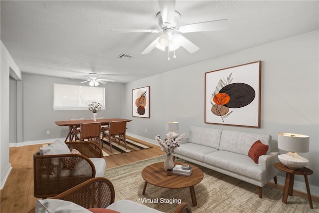 living room with ceiling fan, a textured ceiling, and light wood-type flooring