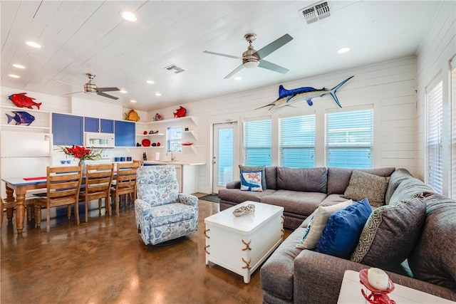 living room with ceiling fan, visible vents, and finished concrete floors