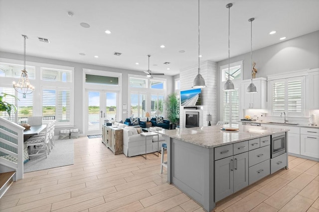 125 Reserve Ln, Rockport, TX 78382 - kitchen with ceiling fan, stainless steel microwave, gray cabinets, a kitchen island, and light wood-style flooring