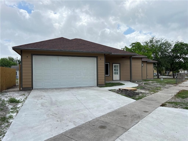 ranch-style house featuring fence, an attached garage, concrete driveway, and a shingled roof