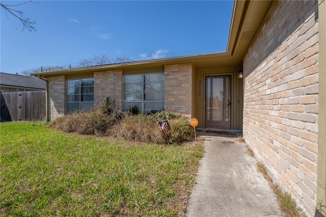 view of exterior entry with a yard and brick siding