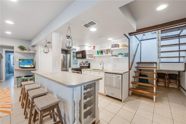 kitchen featuring a breakfast bar, a sink, visible vents, appliances with stainless steel finishes, and open shelves