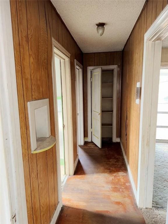 corridor with a textured ceiling, wood walls, and light wood finished floors