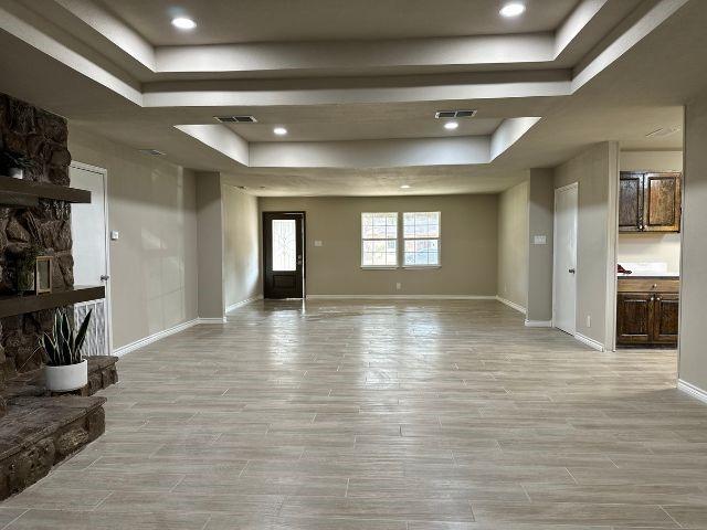 1501 Rose Dr, Alice, TX 78332 - unfurnished living room with a raised ceiling, light wood-style floors, a stone fireplace, and recessed lighting