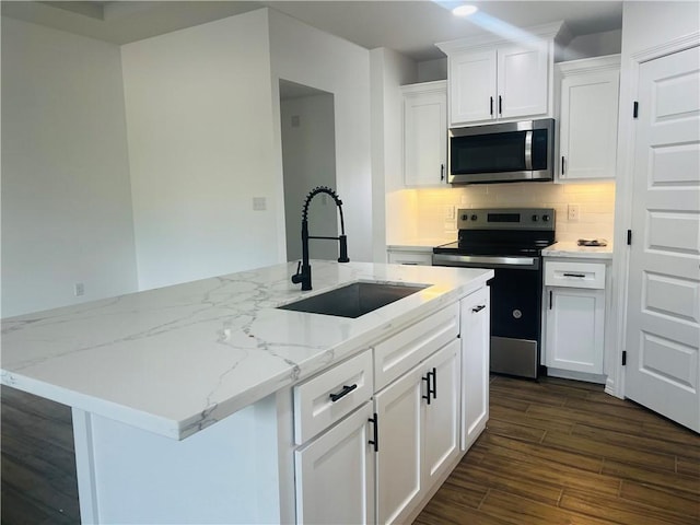 kitchen with light stone countertops, appliances with stainless steel finishes, sink, white cabinets, and a center island with sink