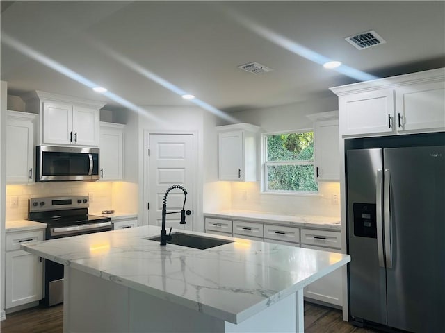 kitchen with sink, white cabinets, stainless steel appliances, and an island with sink