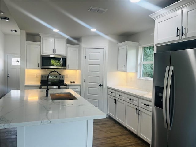 kitchen featuring light stone counters, white cabinetry, appliances with stainless steel finishes, and a kitchen island with sink