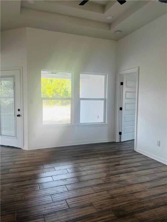 empty room with dark wood-type flooring, a healthy amount of sunlight, ceiling fan, and a raised ceiling