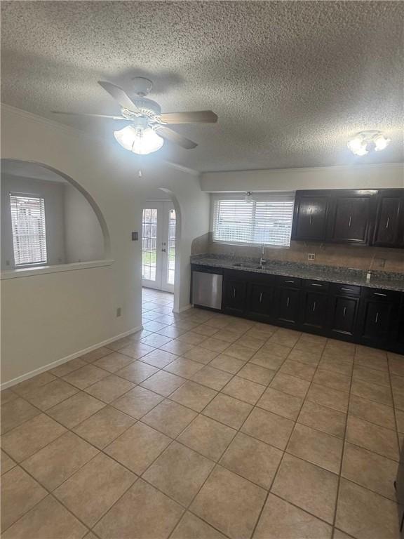 kitchen featuring arched walkways, ceiling fan, light tile patterned floors, stainless steel dishwasher, and dark cabinetry