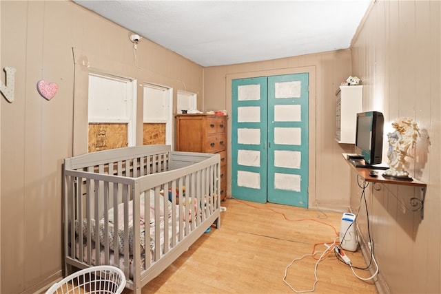 bedroom featuring a crib, light wood-type flooring, wood walls, and french doors