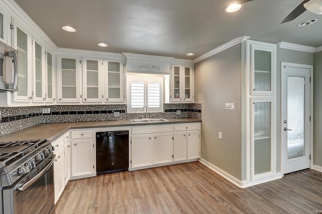 kitchen featuring stainless steel appliances, dark countertops, light wood-style flooring, white cabinets, and a sink