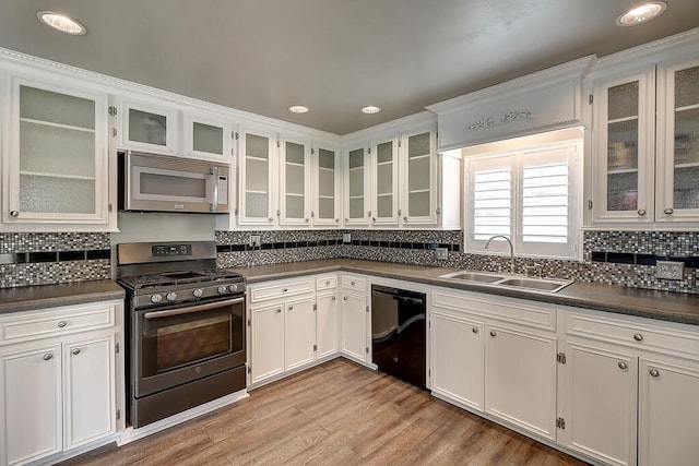 kitchen featuring stainless steel appliances, dark countertops, a sink, and light wood-style flooring