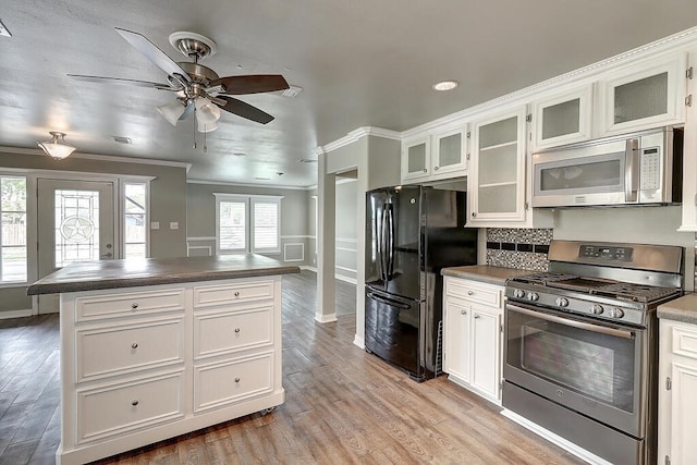 kitchen with white cabinets, ornamental molding, appliances with stainless steel finishes, light wood finished floors, and dark countertops