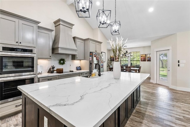 kitchen with tasteful backsplash, lofted ceiling, sink, stainless steel appliances, and custom range hood