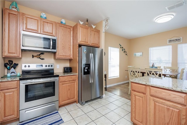 kitchen with light stone counters, light brown cabinets, light tile patterned floors, and appliances with stainless steel finishes