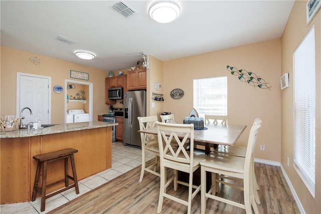 kitchen with washing machine and clothes dryer, light stone countertops, sink, stainless steel appliances, and light wood-type flooring