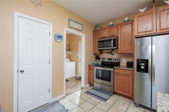 kitchen with light stone countertops, appliances with stainless steel finishes, washer / dryer, and light tile patterned flooring