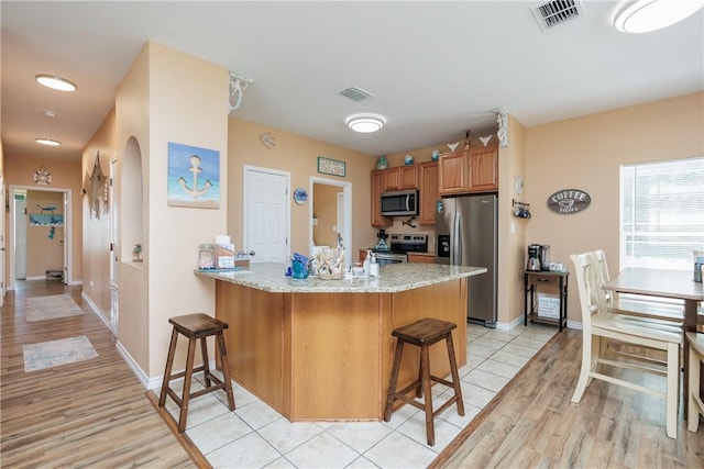 kitchen with a kitchen breakfast bar, light stone countertops, appliances with stainless steel finishes, light hardwood / wood-style floors, and kitchen peninsula