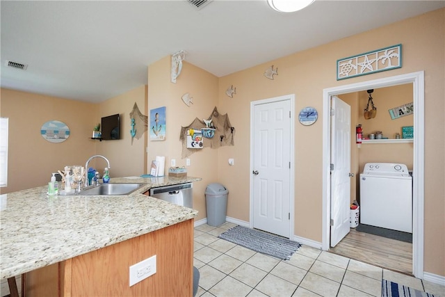 kitchen with kitchen peninsula, sink, light tile patterned floors, dishwasher, and washer / clothes dryer