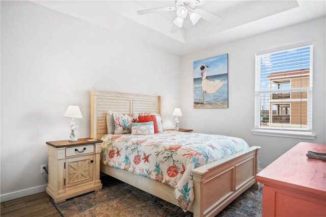 bedroom with dark wood finished floors, baseboards, a tray ceiling, and a ceiling fan