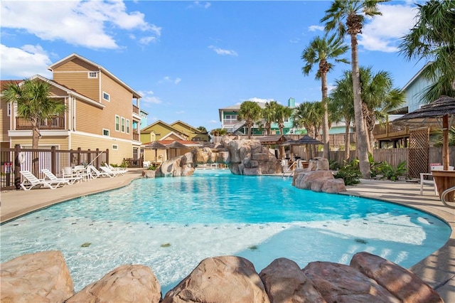 community pool with a patio area, a water slide, and fence