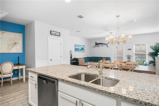 kitchen featuring open floor plan, stainless steel dishwasher, light wood-style floors, white cabinets, and a sink