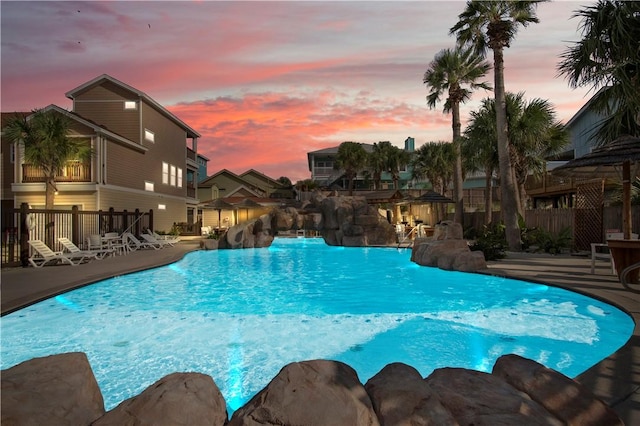 pool at dusk featuring a patio area, a community pool, a water slide, and fence