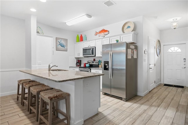 kitchen featuring visible vents, a sink, a kitchen breakfast bar, stainless steel appliances, and white cabinets