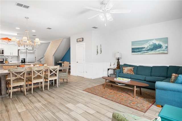 living area featuring visible vents, light wood-style flooring, and ceiling fan with notable chandelier