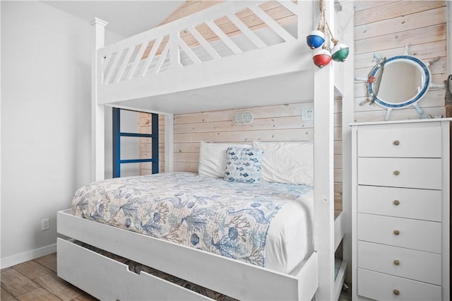 bedroom featuring wooden walls, baseboards, and wood finished floors