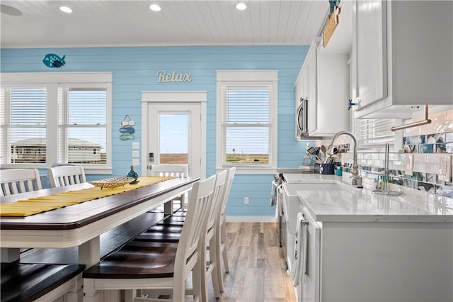 kitchen with a breakfast bar area, white cabinetry, wooden walls, and light hardwood / wood-style floors