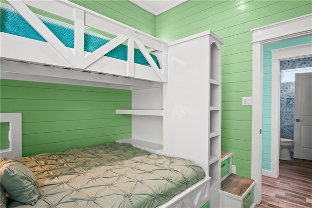 bedroom featuring ensuite bath, wood walls, and hardwood / wood-style floors