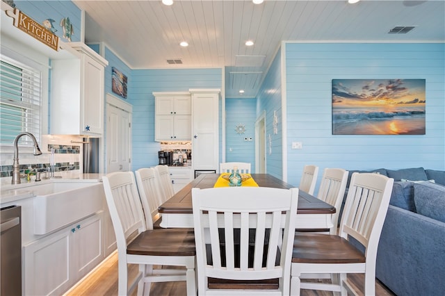 dining area with sink, wooden walls, and light hardwood / wood-style flooring