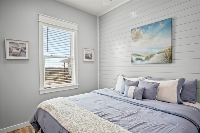 bedroom with multiple windows, wood walls, and hardwood / wood-style flooring