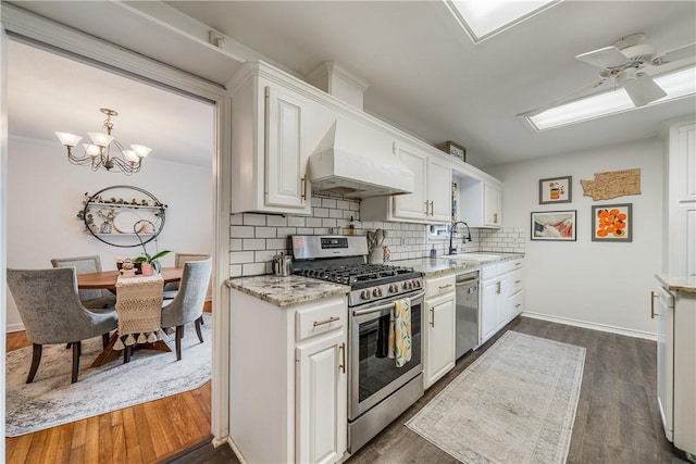 622 Bermuda Pl, Corpus Christi, TX 78411 - kitchen with stainless steel appliances, wall chimney range hood, a ceiling fan, white cabinets, and decorative backsplash