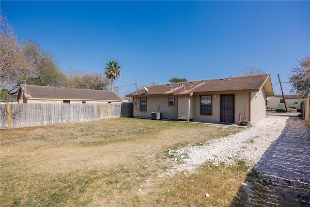 back of property with central AC, a lawn, fence, and stucco siding