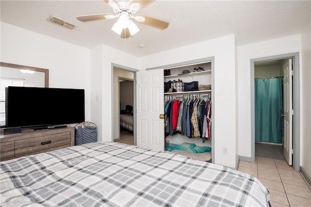 bedroom featuring light tile patterned floors, a closet, visible vents, a ceiling fan, and a textured ceiling