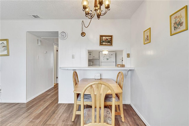 dining space featuring wood-type flooring, a textured ceiling, and a chandelier