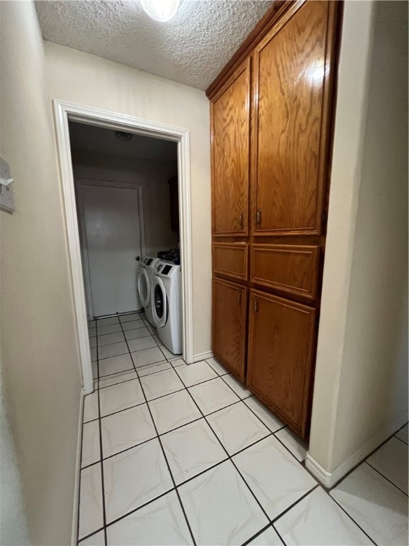 washroom with a textured ceiling, washer and clothes dryer, and light tile patterned flooring