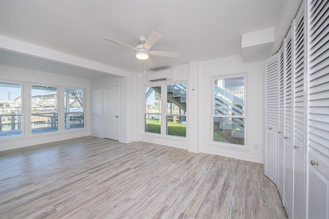 interior space with a wall unit AC, ceiling fan, and light wood-type flooring