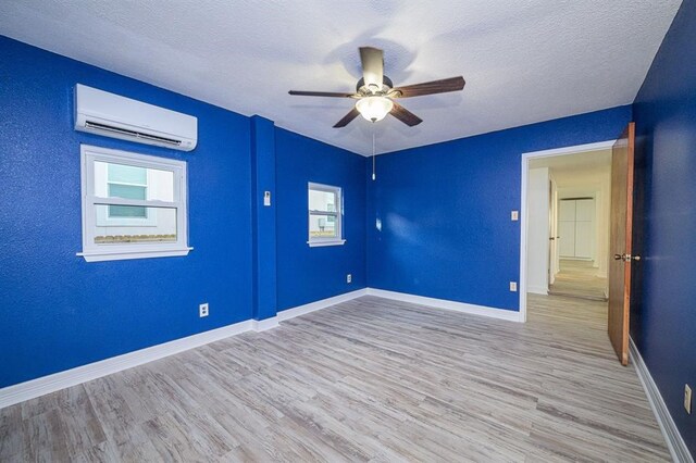 unfurnished room with ceiling fan, light hardwood / wood-style floors, a textured ceiling, and a wall mounted AC