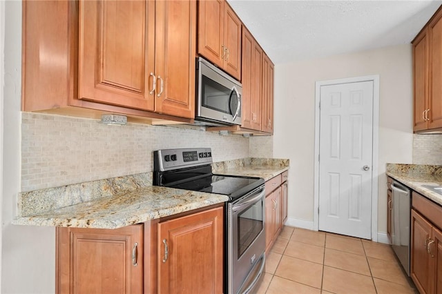 kitchen with appliances with stainless steel finishes, light tile patterned floors, light stone countertops, and decorative backsplash