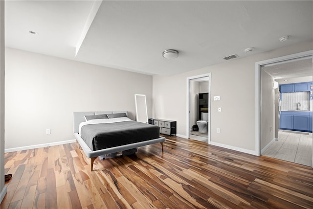 bedroom featuring hardwood / wood-style flooring, ensuite bath, and sink