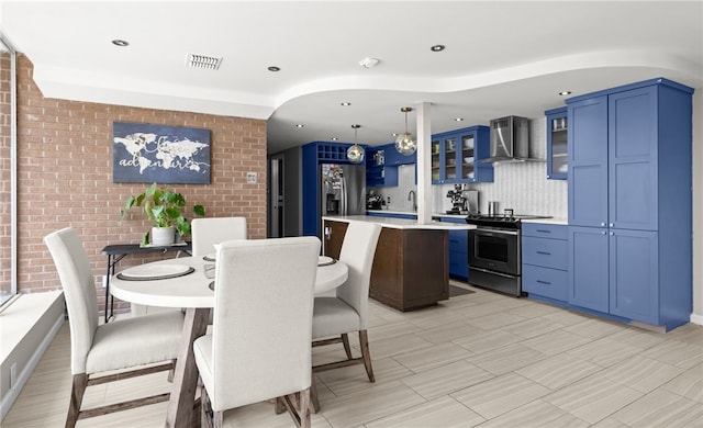 kitchen with wall chimney exhaust hood, stainless steel appliances, blue cabinets, decorative light fixtures, and a kitchen island